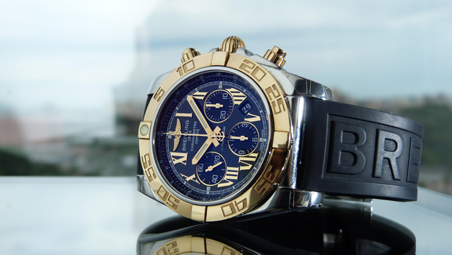 Breitling Chronograph mit blauem Zifferblatt, goldener Lünette und schwarzem Kautschukarmband.