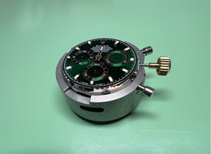 Rolex Uhrwerk mit grünem Zifferblatt und goldener Krone in einer Haltevorrichtung – Detailansicht für Identifikation und Prüfung