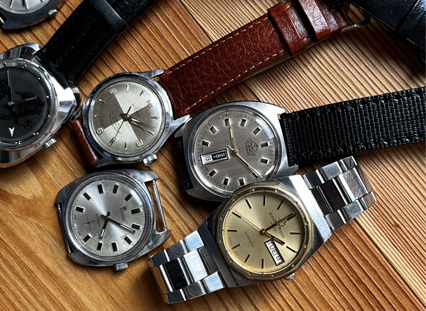Mehrere Vintage-Armbanduhren mit unterschiedlichen Armbändern und Zifferblättern auf Holztisch – Symbolfoto für den Verkauf eines Uhrenkonvoluts